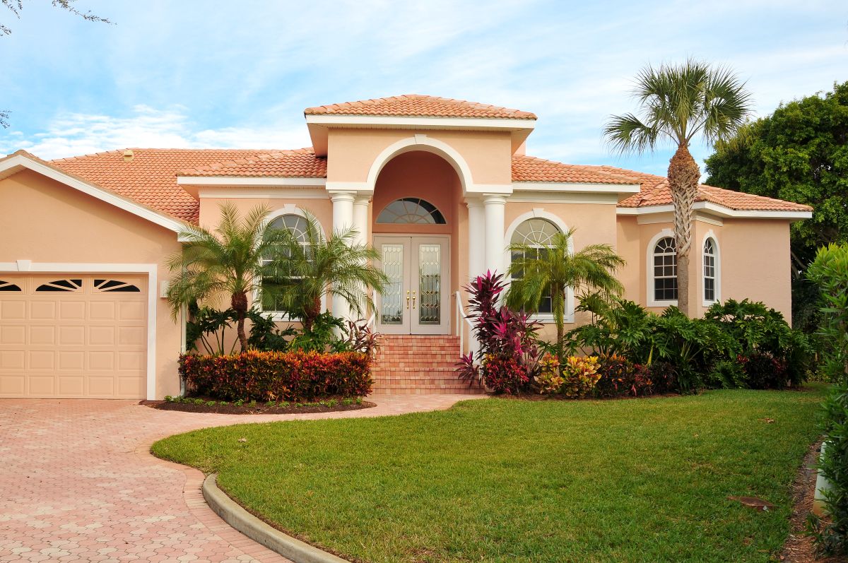 Elegant home, with huge archway covering double door entrance,  flanking columns, lush tropical landscaping.